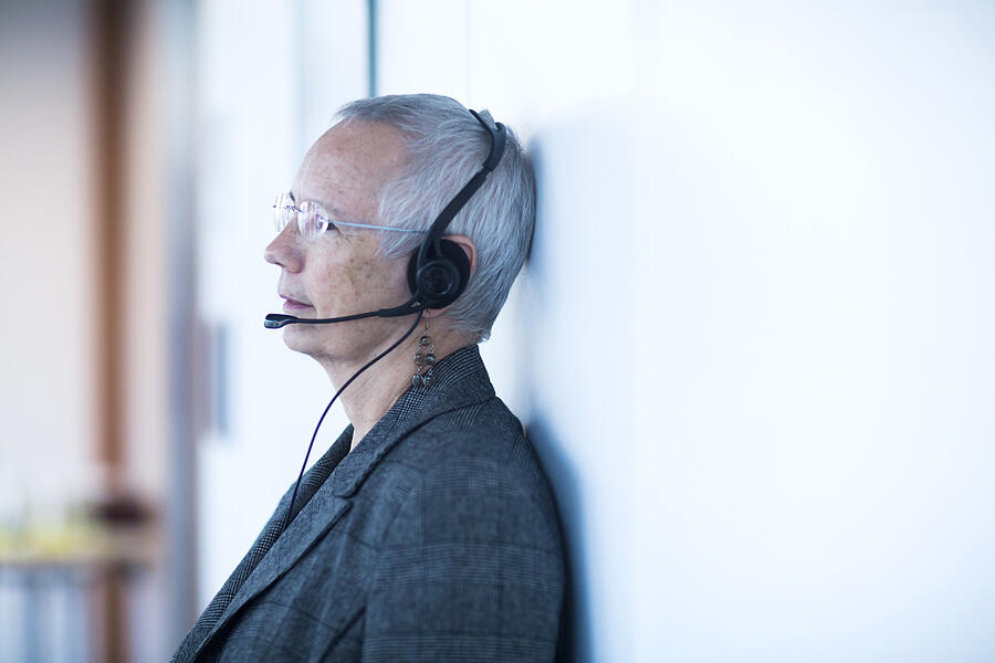 Side view of mature woman leaning against wall wearing telephone headset looking away Photograph by Sigrid Gombert