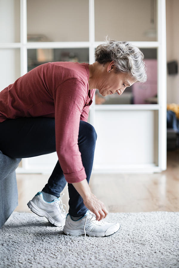 Side view of mature woman tying shoelace at home Photograph by Cavan Images