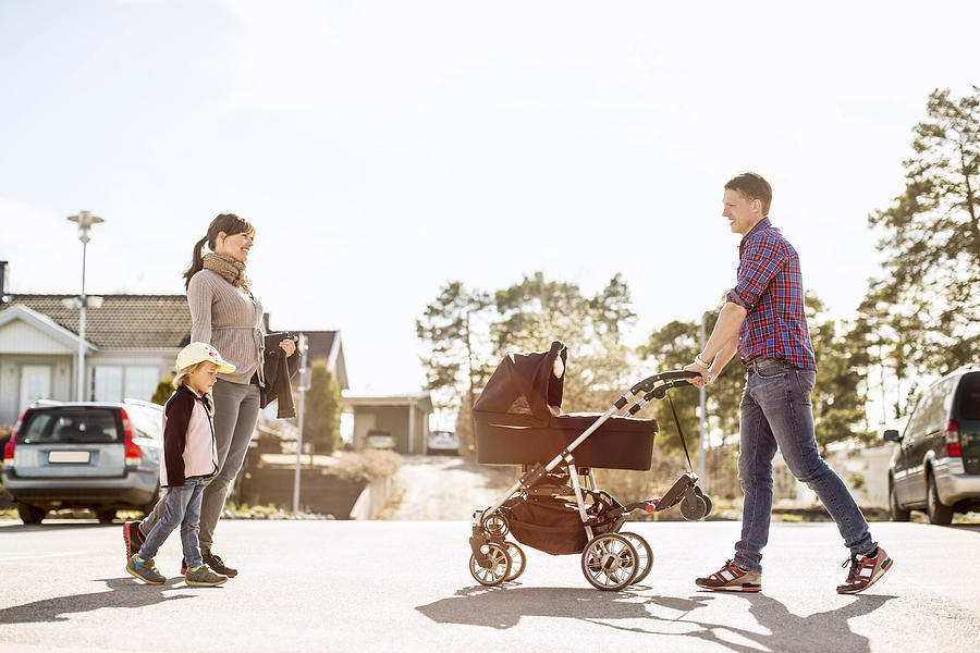 Side view of parents with baby carriage and daughter walking on street Photograph by Maskot