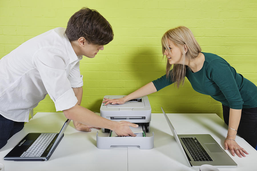 Side view of young businesspeople setting up printer with laptops at desk Photograph by Moodboard