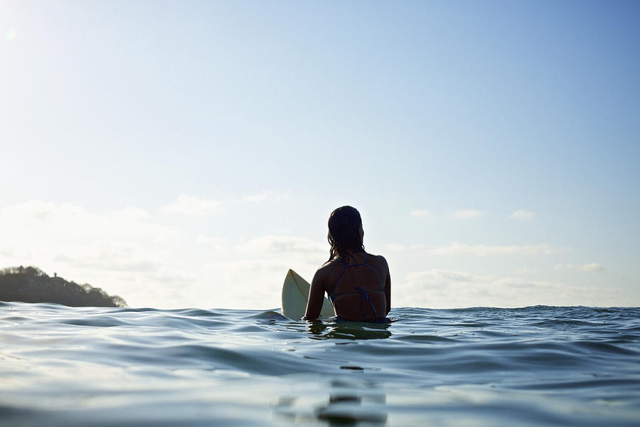 Silhouette female surfer straddling surfboard, waiting in sunny blue ocean Photograph by Nik West