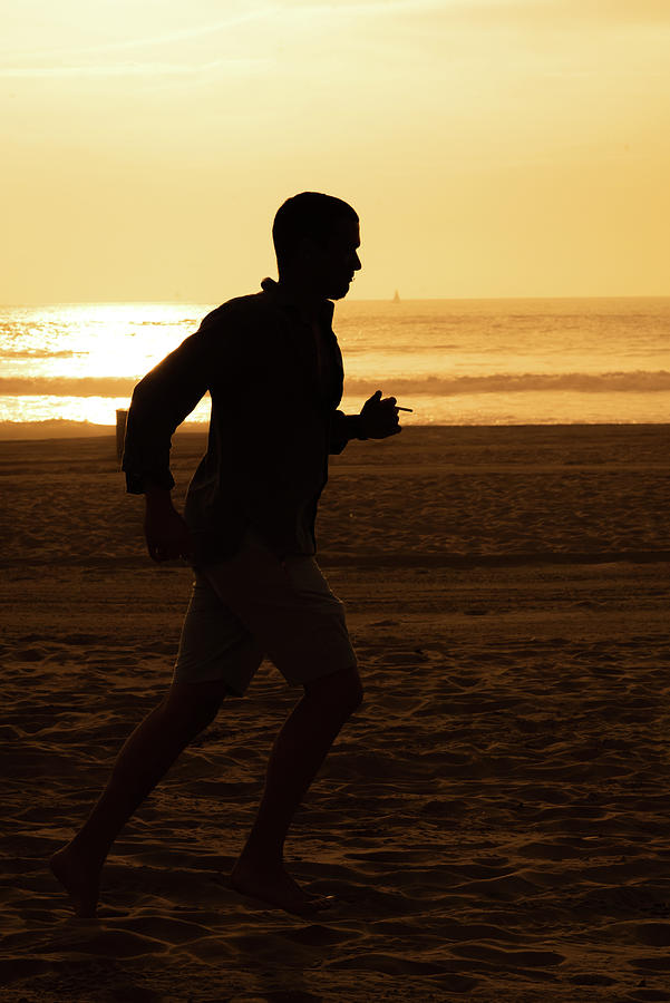 Silhouette of a tall man running on beach at sunset stock photo Photograph by Mark Stout