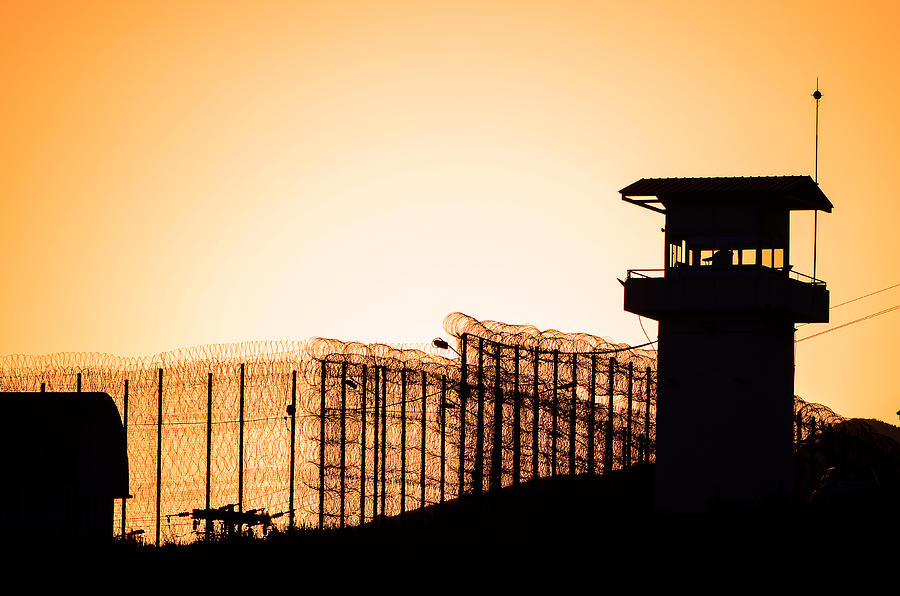 Silhouette of barbed wires and watchtower of prison. Photograph by Gatsi