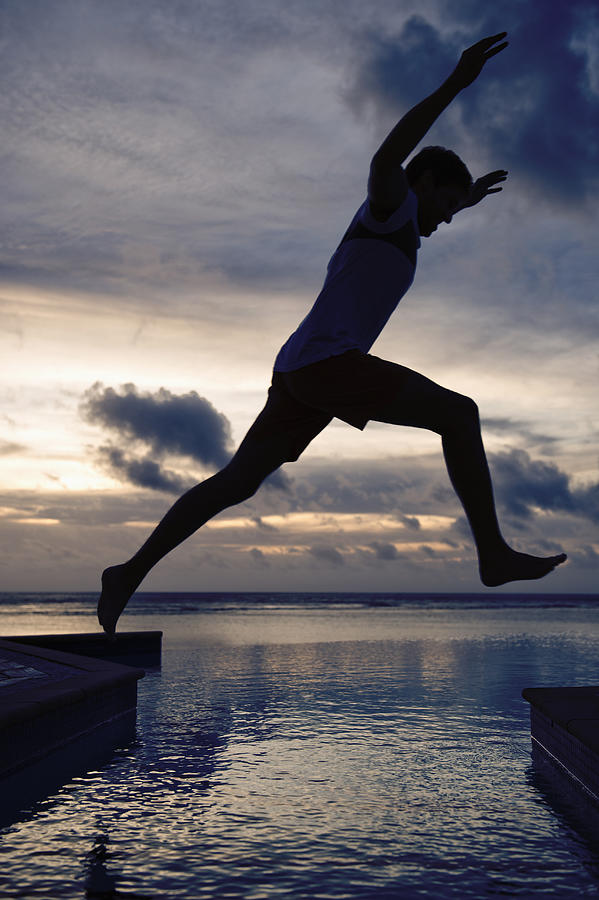 Silhouette of Caucasian man jumping over swimming pool at sunset Photograph by Jacobs Stock Photography Ltd