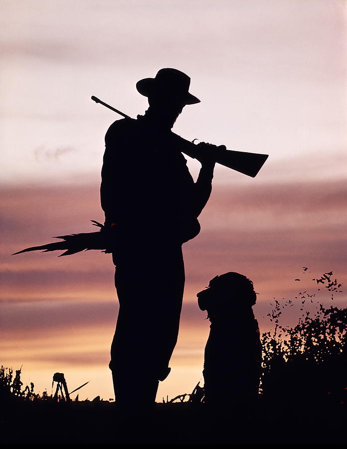 Silhouette Of Man Hunter, Holding Rifle Or Gun, Wearing Cowboy Hat And Standing With Dog In Field. Sunset Is Behind. Photograph by H. Armstrong Roberts