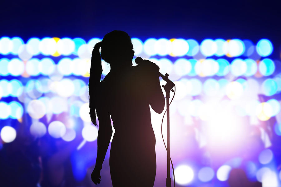 Silhouette of woman with microphone singing on concert stage in front of crowd Photograph by FangXiaNuo