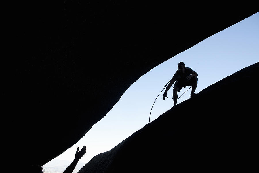 Silhouette of young male climbers reaching out for each other on rock Photograph by Zero Creatives