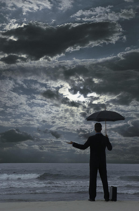 Silhouetted Businessman Standing on a Beach at Night, Holding an Umbrella and Checking for Rain Photograph by John Cumming