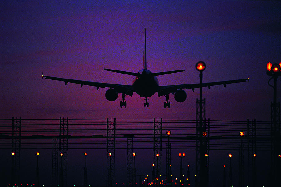 Silhouetted plane landing at night Photograph by Digital Vision.