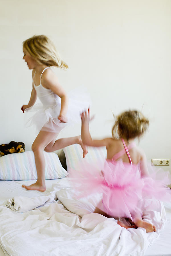 Sisters dressed as ballet dancers running on bed Photograph by Emely