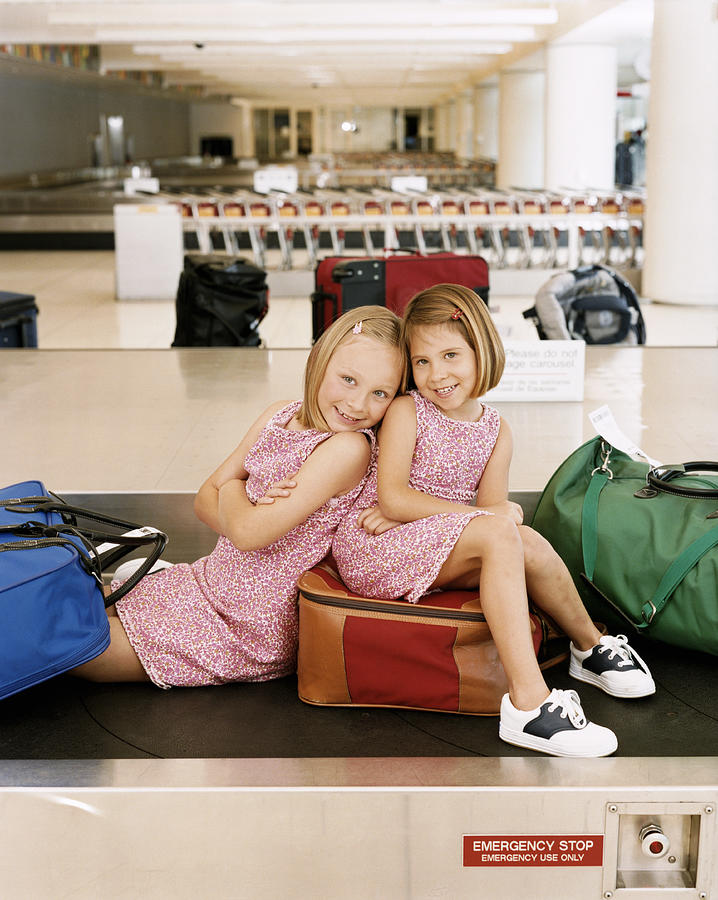 Sisters Sitting on Suitcases at Airport Baggage Collection Photograph by Digital Vision.