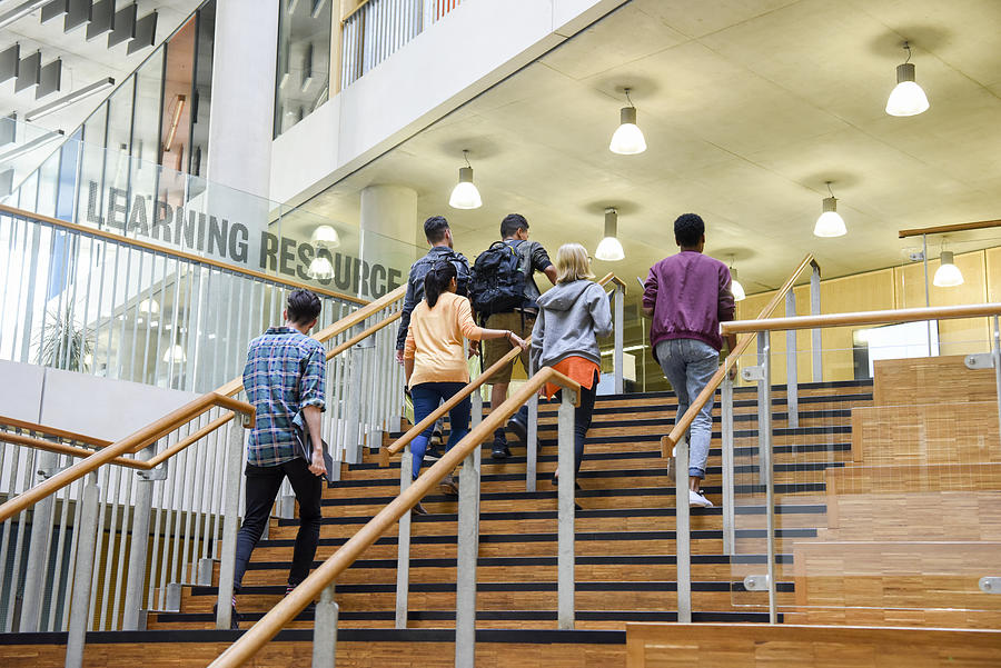 Six students walking up wooden steps in modern college building Photograph by JohnnyGreig