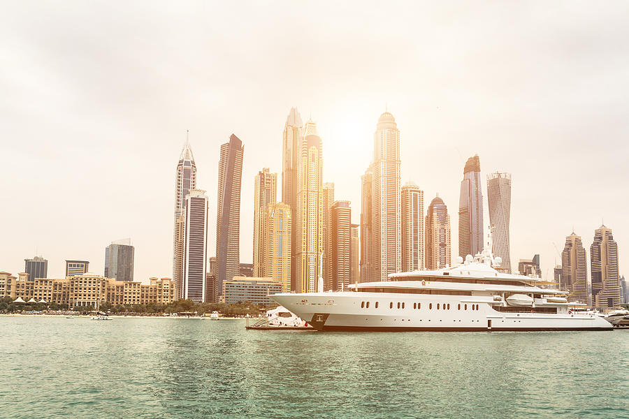 Skyline of Dubai from sea at sunset with a luxury yacht in foreground Photograph by PJPhoto69