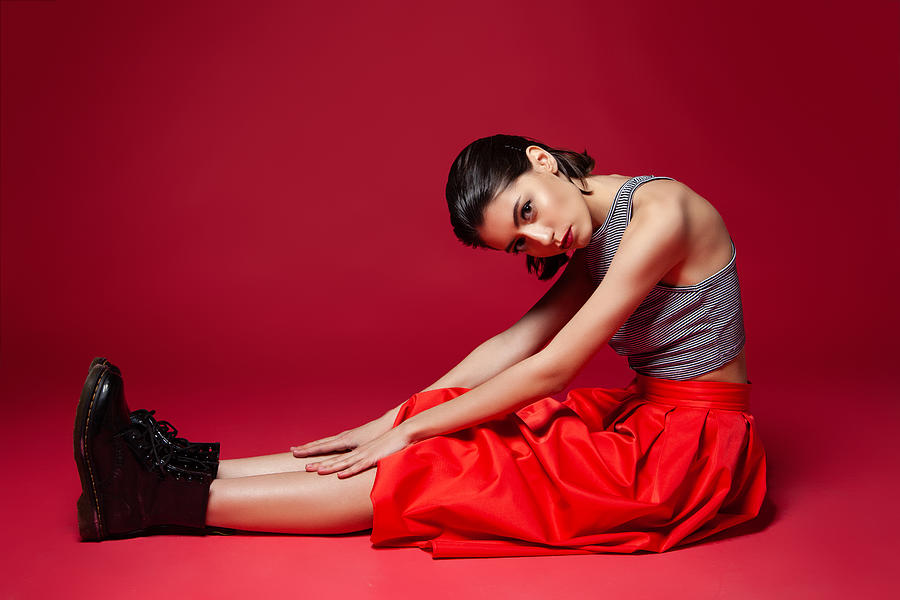 Slender stylish female sitting on red background Photograph by Iuliia Isaieva