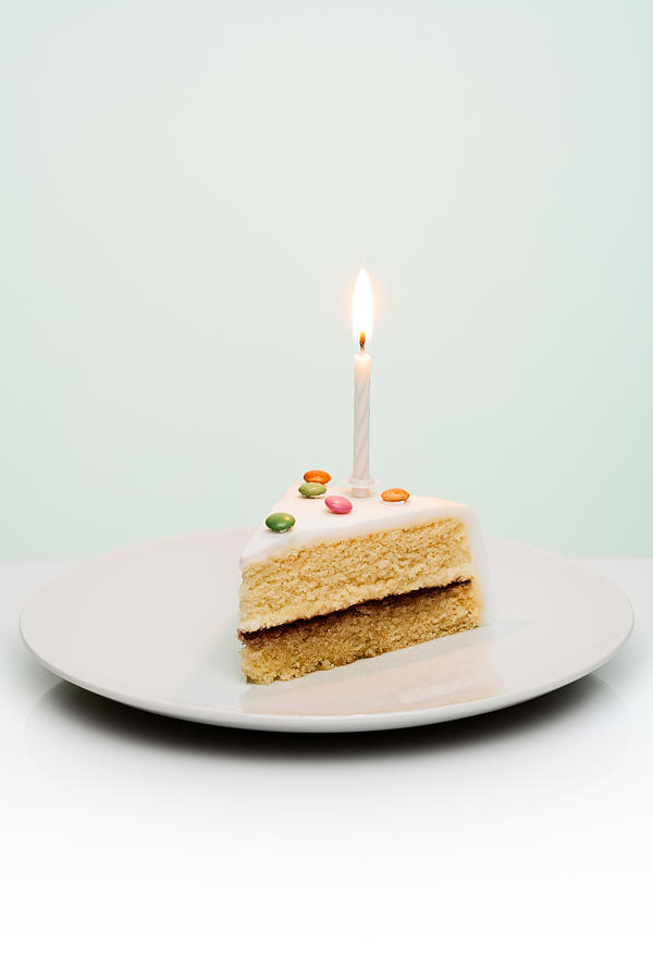 Slice of birthday cake with candle sticking out of Photograph by Creative Crop
