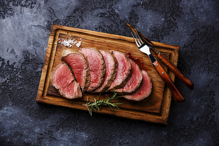 Sliced grilled tenderloin Steak roastbeef on wooden cutting board on dark background Photograph by The Picture Pantry