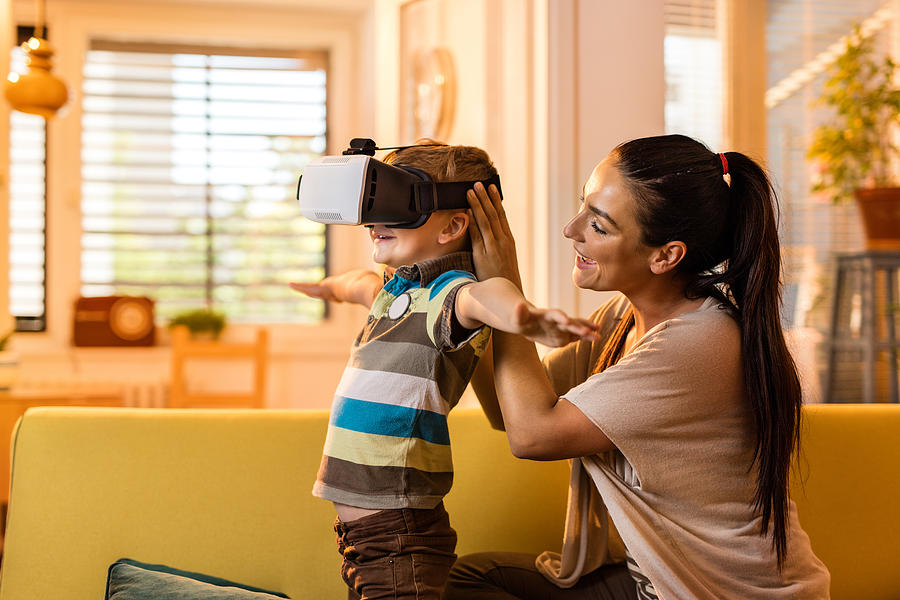 Small boy using virtual reality glasses with his mother. Photograph by Skynesher