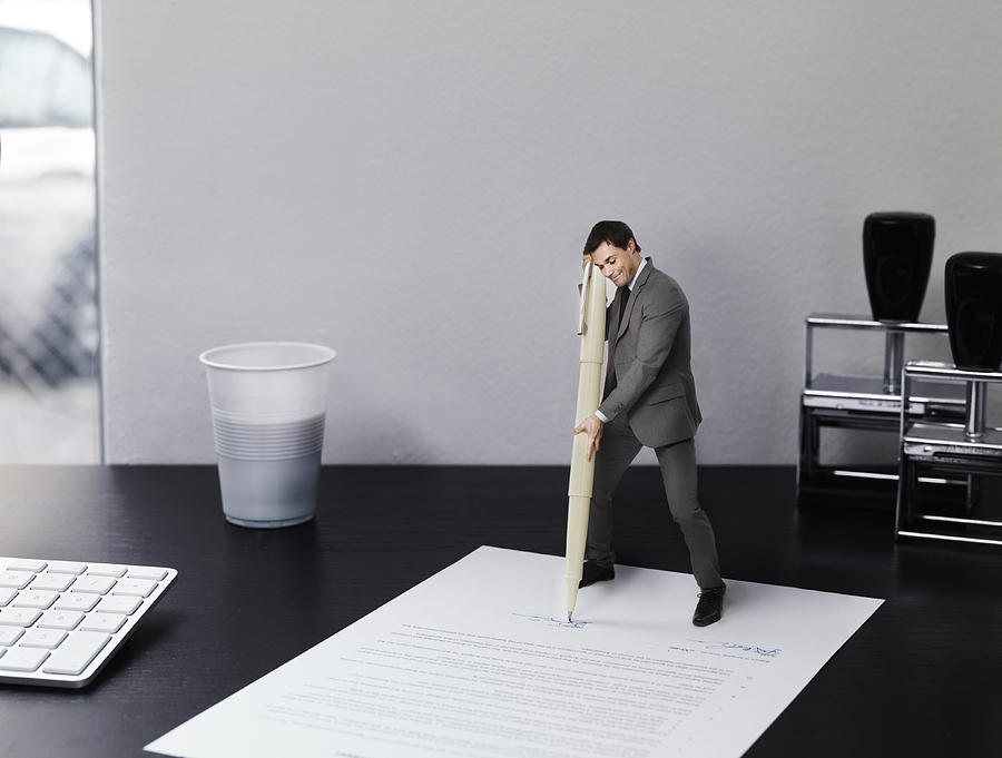 Small businessman signing document on office desk Photograph by Henrik Sorensen