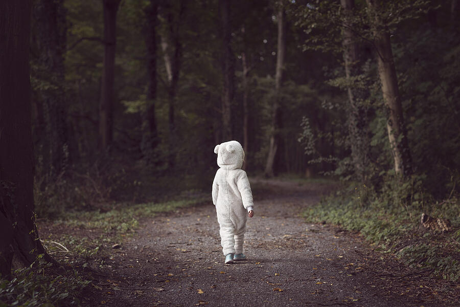 Small child wearing white bear suit, walking along a tree-lined forest path Photograph by Elva Etienne