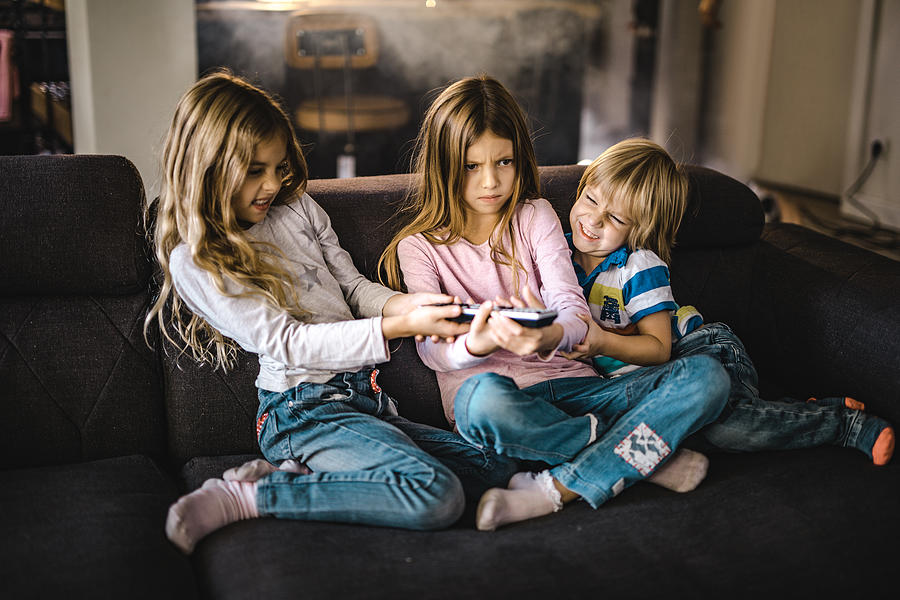 Small siblings fighting over a remote control in the living room. Photograph by Skynesher