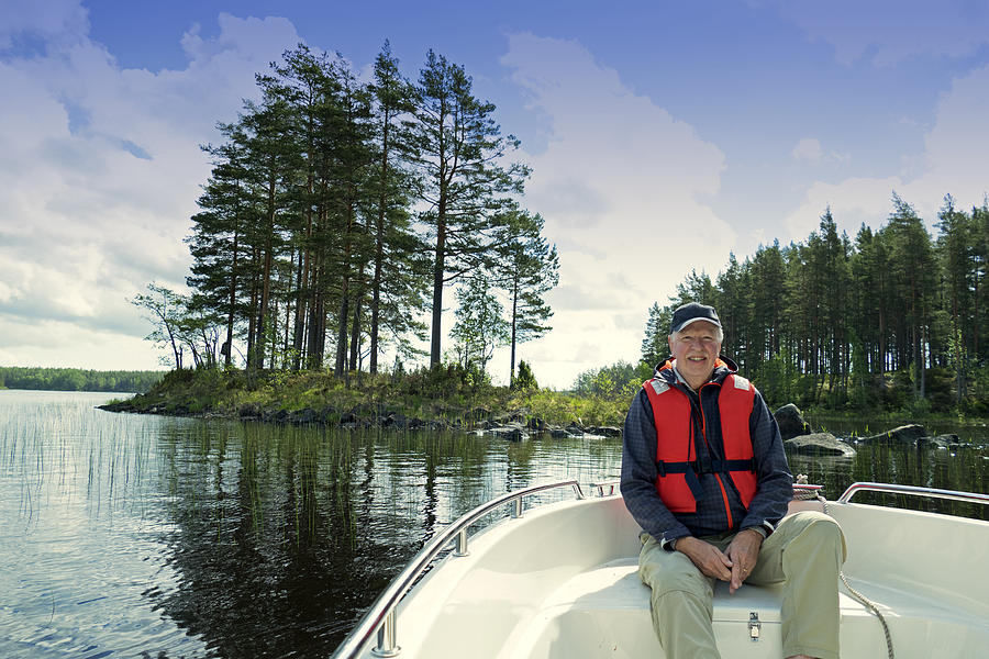 Smiling 73 years old senior wearing  a cap and a life jacket sitting in front of a motorboat sailing in Gastrikland,Sweden Photograph by Brytta