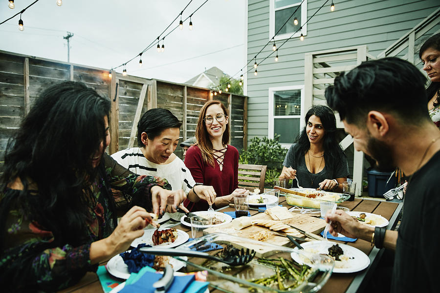 Smiling and laughing friends sharing dinner at table in backyard Photograph by Thomas Barwick