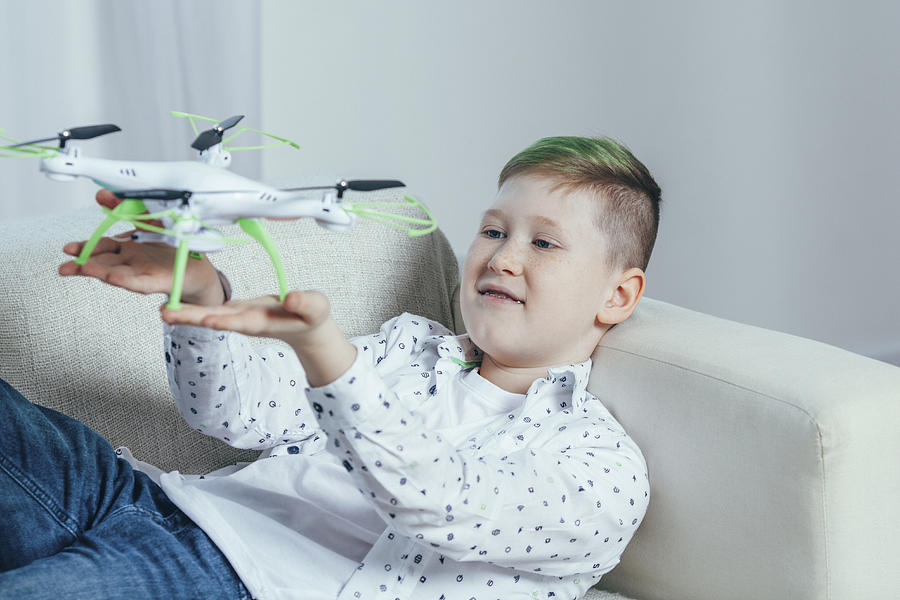 Smiling boy lying on sofa holding drone in living room at home Photograph by Vasily Pindyurin
