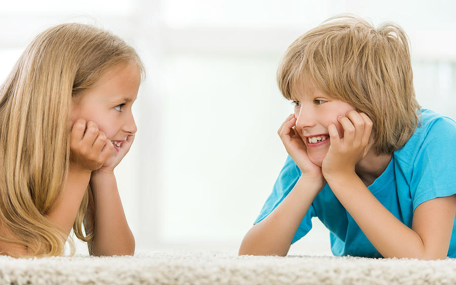 Smiling brother and sister lying on the carpet and talking. Photograph by Skynesher