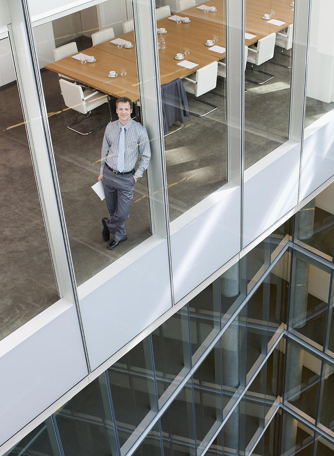 Smiling businessman leaning against window in conference room Photograph by Chris Ryan