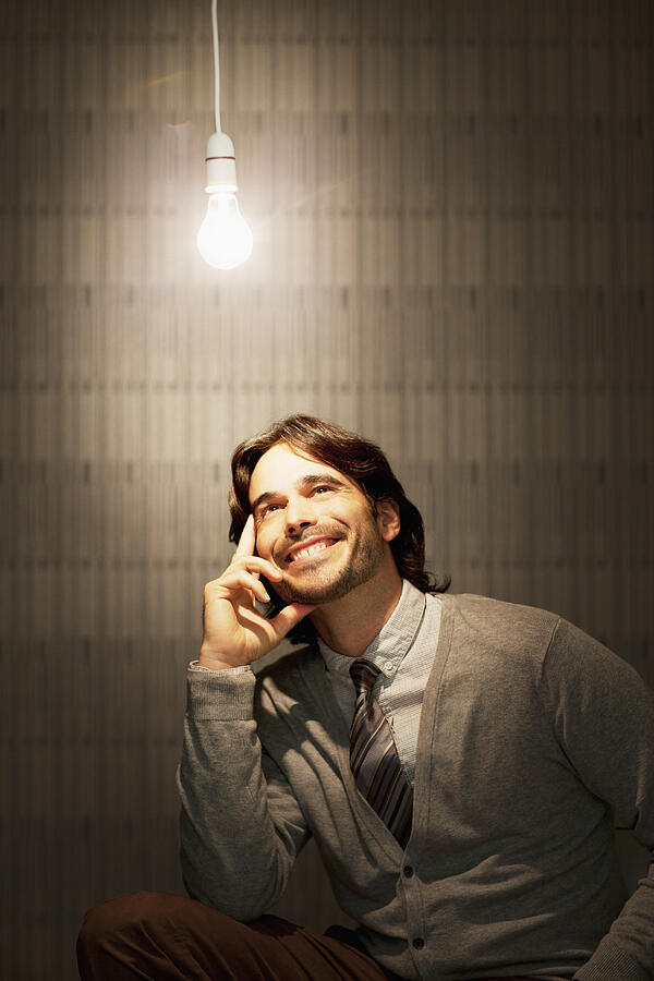 Smiling businessman sitting under illuminated light bulb Photograph by Sam Edwards