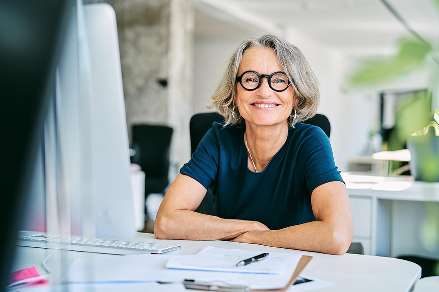 Smiling businesswoman at desk in office Photograph by Portra Smiling businesswoman at desk in office Photograph by Portra