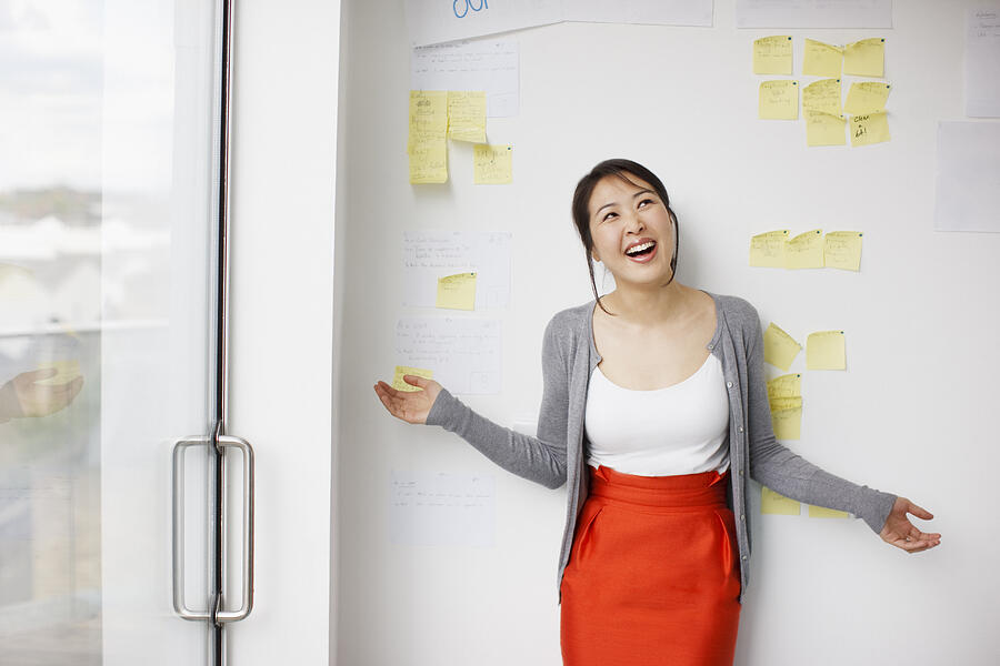 Smiling businesswoman with arms outstretched in front of whiteboard with adhesive notes Photograph by Paul Bradbury