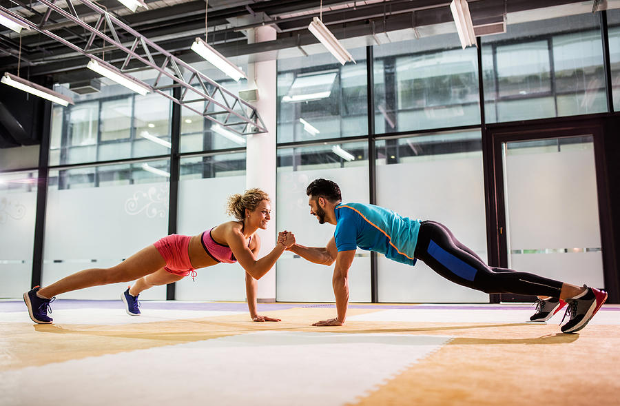 Smiling couple doing push-ups together in a gym. Photograph by Skynesher