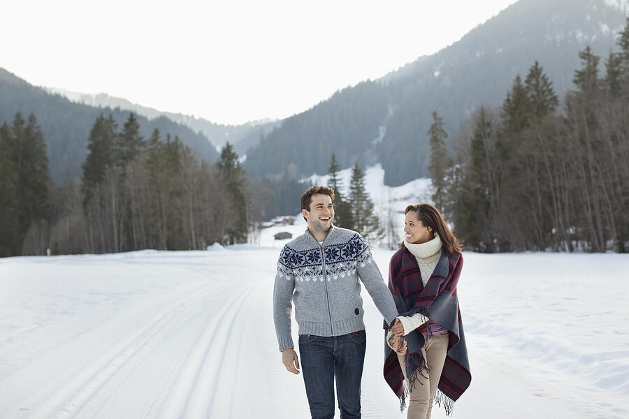 Smiling couple holding hands and walking in snowy field Photograph by Sam Edwards