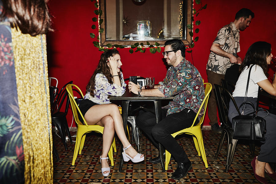 Smiling couple in discussion while seated at table in night club Photograph by Thomas Barwick