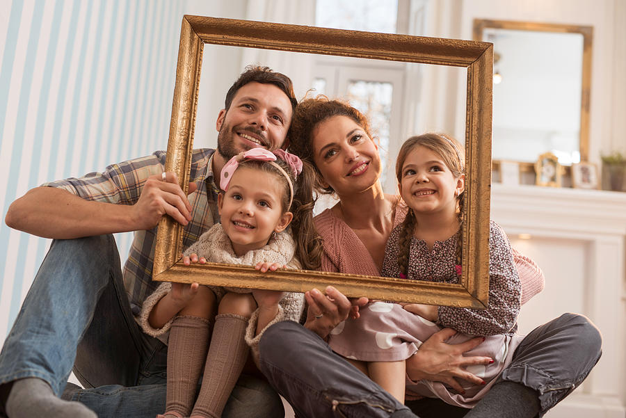 Smiling family having fun with a picture frame at home. Photograph by BraunS