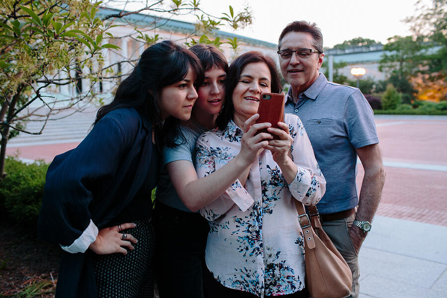 Smiling family looking at smartphone in outdoor setting Photograph by Stephanie Noritz
