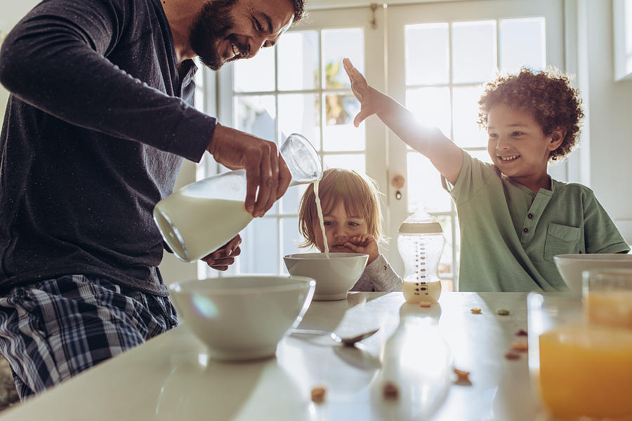 Smiling father pouring milk in to bowls for breakfast Photograph by Jacoblund