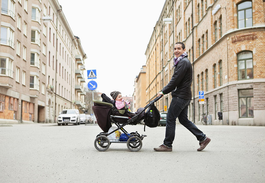 Smiling father walking with cute baby (0-11 months) in stroller Photograph by Maskot