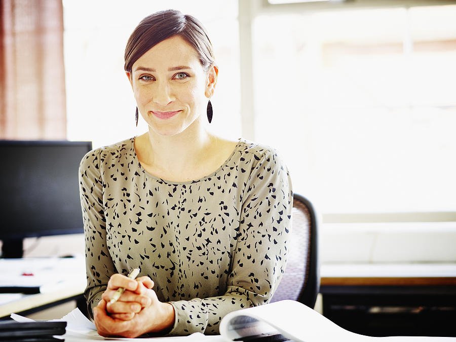 Smiling female businesswoman seated at workstation Photograph by Thomas Barwick