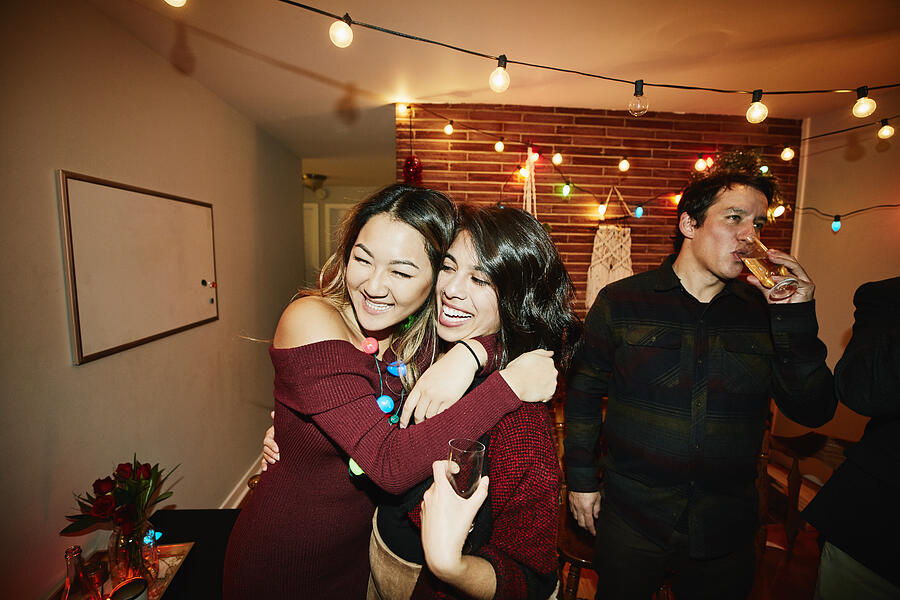 Smiling female friends hugging during holiday party in home Photograph by Thomas Barwick
