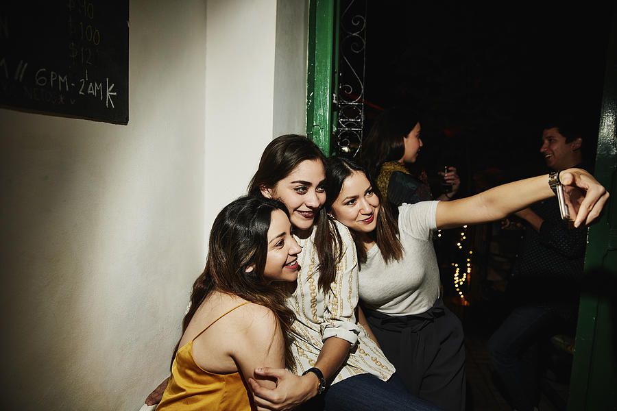 Smiling female friends taking selfie with smart phone while hanging out in night club Photograph by Thomas Barwick