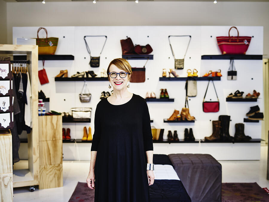 Smiling female shop owner standing in boutique Photograph by Thomas Barwick