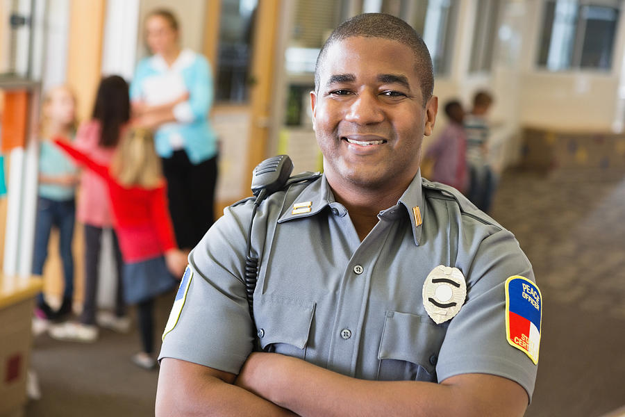 Smiling friendly police officer providing security on school campus Photograph by SDI Productions