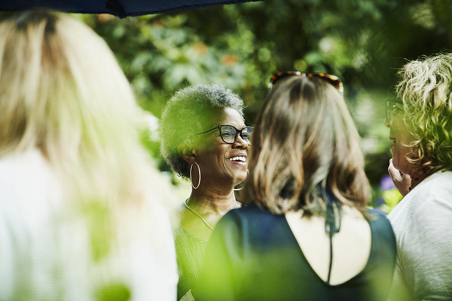 Smiling friends in discussion during backyard garden party Photograph by Thomas Barwick