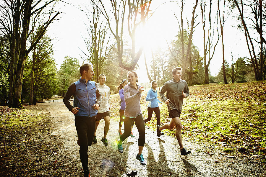 Smiling friends running together in park Photograph by Thomas Barwick