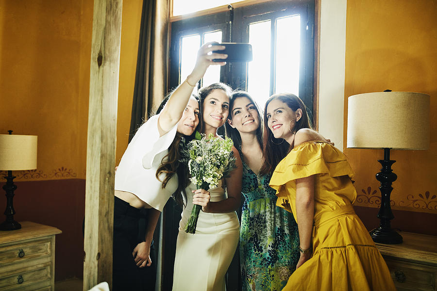 Smiling friends taking a selfie with bride before wedding ceremony Photograph by Thomas Barwick