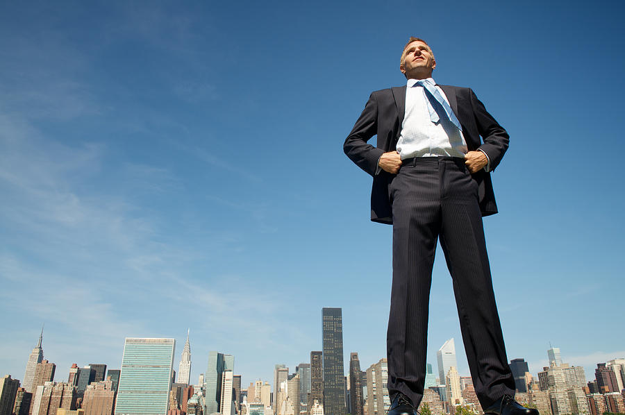 Smiling Giant Businessman Standing Tall and Proud Above City Skyline Photograph by PeskyMonkey