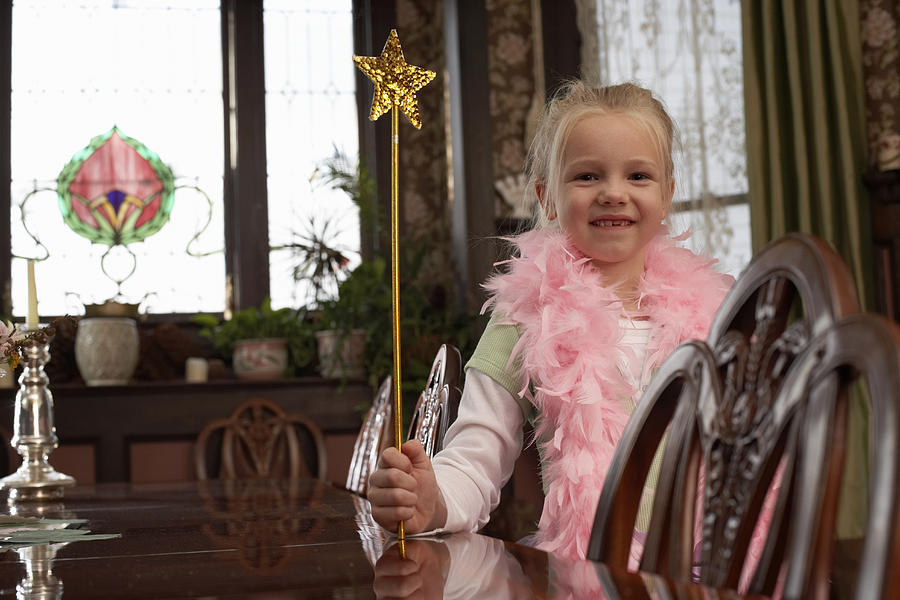Smiling girl (6-7) wearing feather boa holding magic wand in living room Photograph by Christopher Robbins