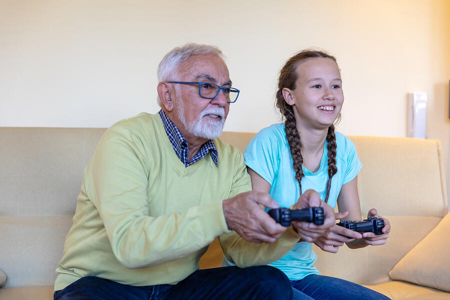 Smiling Girl and her Grandfather are Playing Video Games Together at Home. Photograph by ProfessionalStudioImages